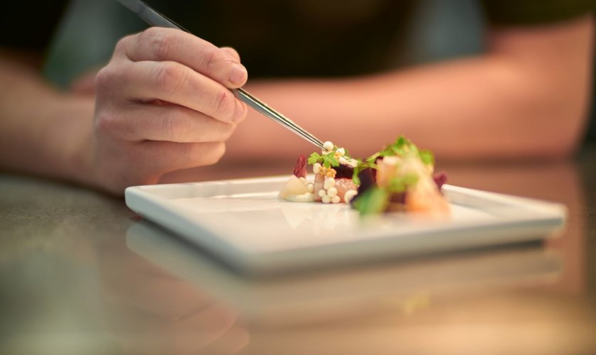 Eine Person dekoriert ein Gourmetgericht auf einem weißen Teller Eine Person dekoriert ein kunstvoll angerichtetes Gourmetgericht auf einem weißen Teller im Restaurant in Stolberg im Harz