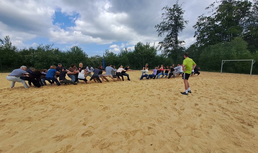 Eine Outdoor Incentives Aktiviät einer Firma. Die Mitarbeiter machen Tauziehen auf dem sandigen Volleyballfeld.