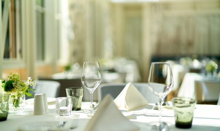 Ein heller, eleganter Speisesaal mit Glasdach, stilvoll gedeckten Tischen und einer zentralen Blumendekoration im Restaurant in Stolberg, Harz.